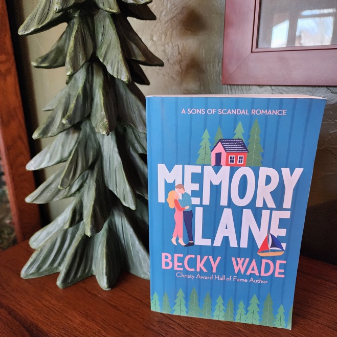 Photo of the paperback copy of Memory Lane by Becky Wade, displayed on the top of a shelf with a tree figurine the the background